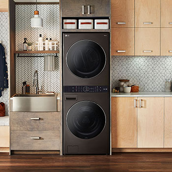 La LG WashTower® WK25BS6 en Black Steel (Lavadora 22 kg, Secadora 22 kg), instalada en un moderno cuarto de lavado con gabinetes de madera.