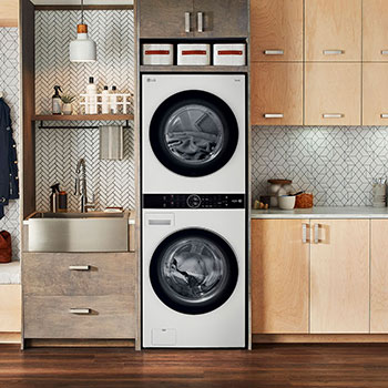 La LG WashTower® WK22WS6E en color blanco (Lavadora 22 kg, Secadora 22 kg), instalada en un moderno cuarto de lavado con gabinetes de madera.