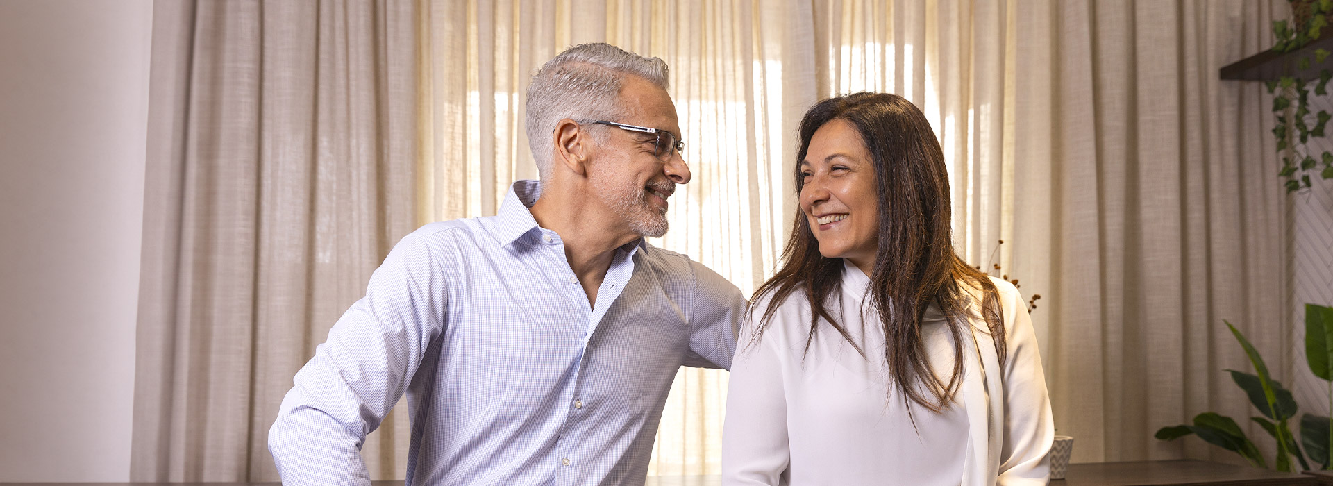 Luis y Rosana sonriéndose el uno al otro, sentados frente a una cortina.