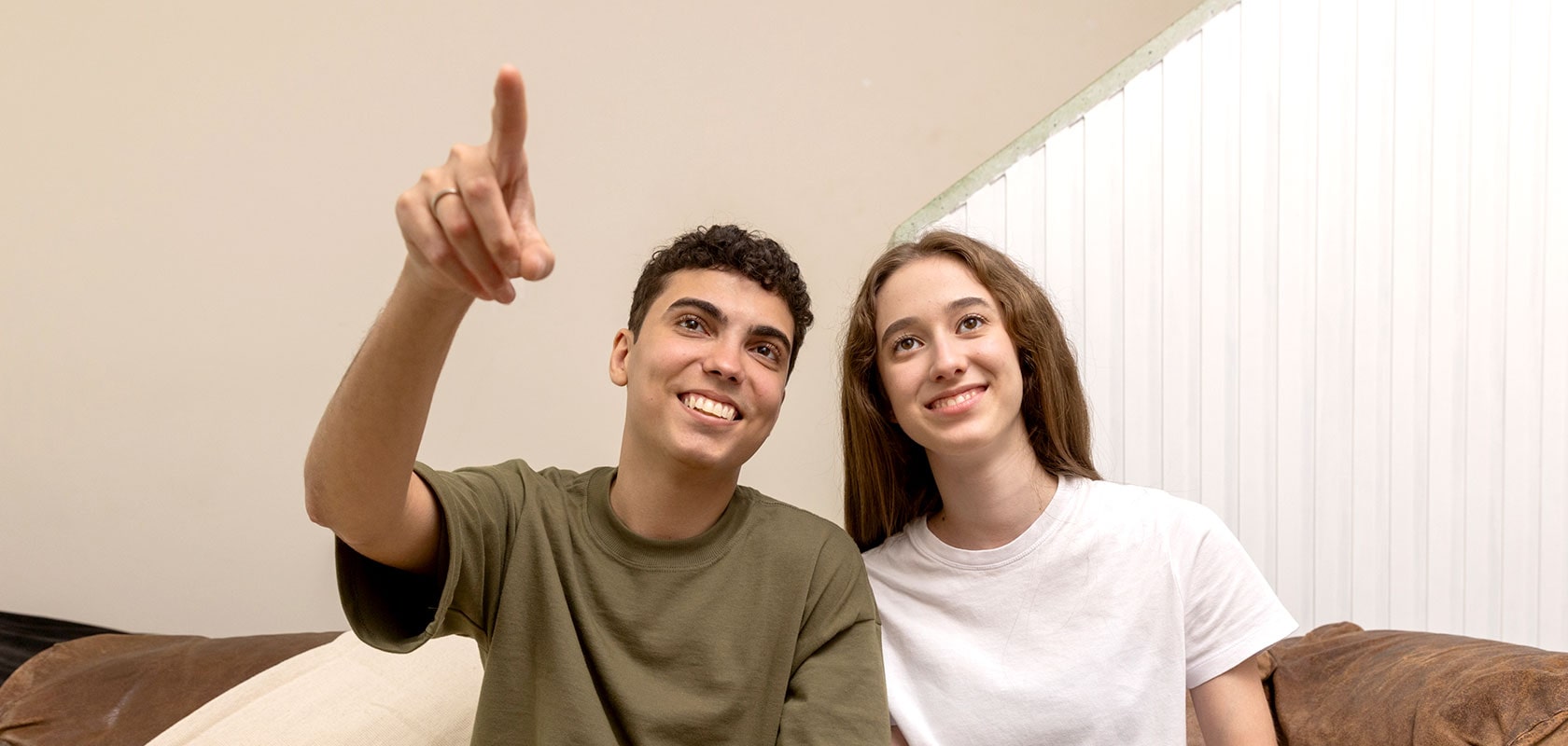 Dos jóvenes sonriendo y haciendo un gesto mientras están sentados en el sofá.