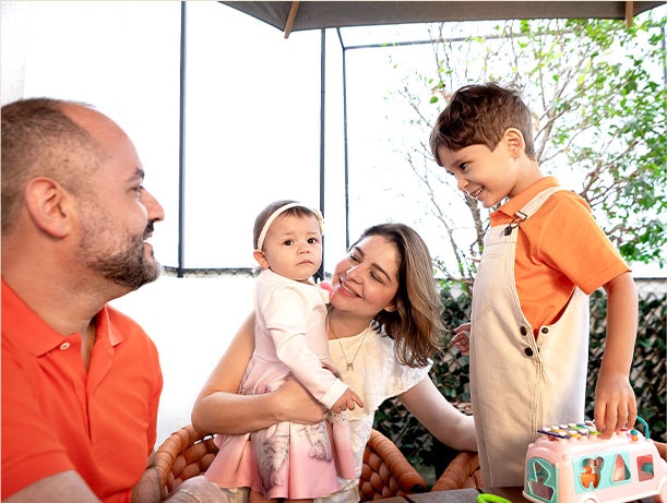 Familia cortada, sonriendo felizmente. Madre sosteniendo a su hijita a sus brazos, padre e hijo también lucen a su linda. Hijo sosteniendo su juguete.