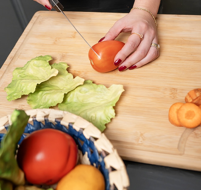 Mamá cortando un tomate rojo. Algunas zanahorias ya han sido cortadas, tomate y otras verduras en el tazón.