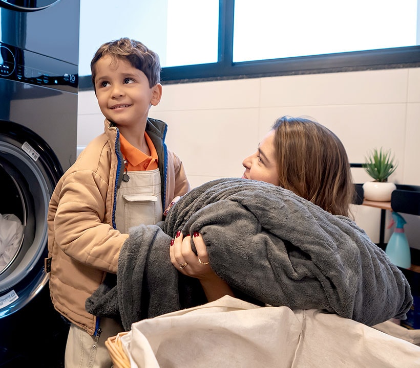 Madre e hijo sosteniendo otra lavandería, una manta oscura grande. Hijo sonriente, alegría de ayudar a su madre. Madre mirando a su hijo con alegría.