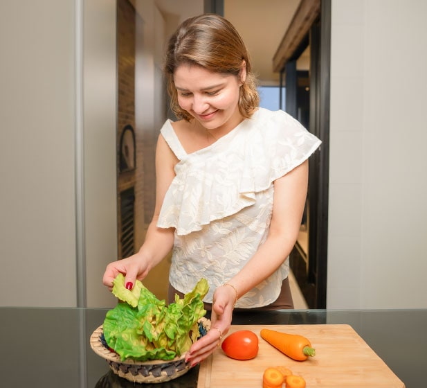 La madre se prepara para la comida, manipulación de ingredientes. Verduras verdes frescas, tomate y zanahorias. Lleva camisas blancas.