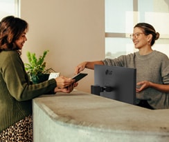 Recepcionista amigable mostrándole a una mujer donde firmar digitalmente en una tablet.