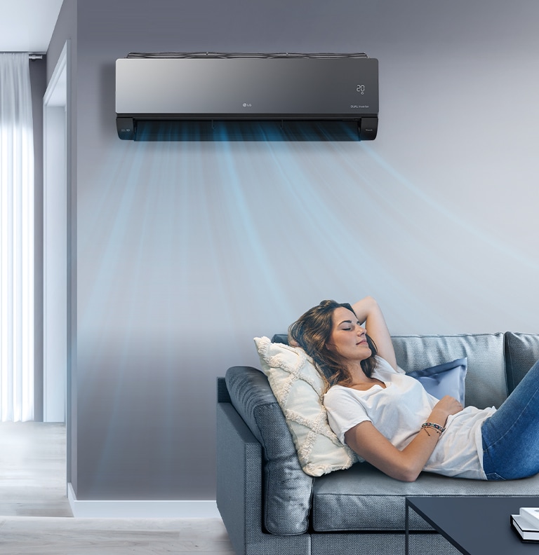 A woman lounges on a couch with the LG AC on the wall above her. Streams of air indicates it is on and cooling the room.