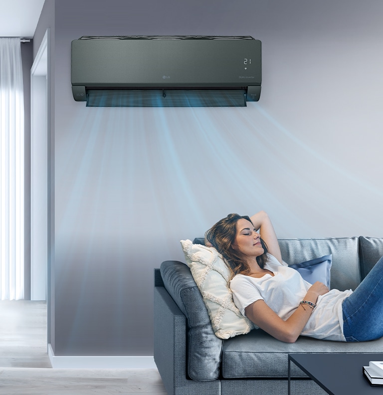 A woman lounges on a couch with the LG AC on the wall above her. Streams of air indicates it is on and cooling the room.