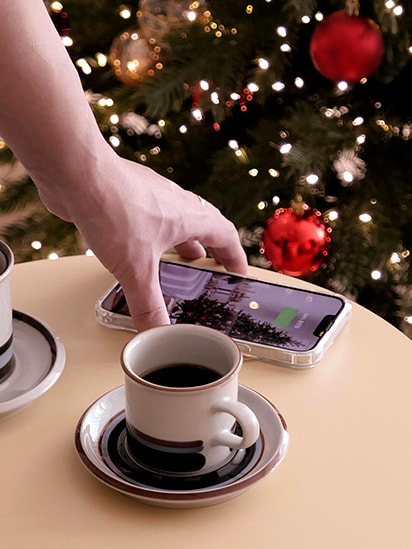 Using the charging function, a cell phone is placed on top of the product. There is a coffee cup next to it, showing it being used like a table.