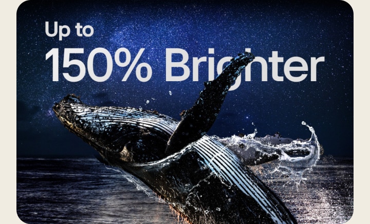 Een stilstaand beeld van een walvis die uit een oceaan springt onder een sterrenhemel. Vervolgens komen de woorden 'Up to 150% brighter' (tot 150% helderder) in beeld op de hemel.