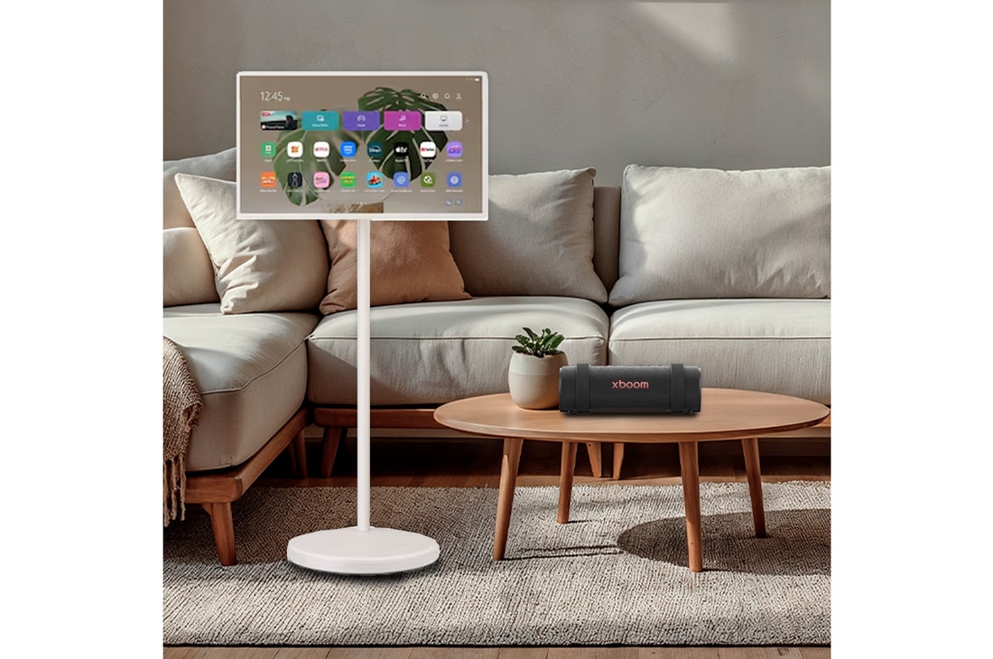 LG StanbyME 2 schermen weergegeven in een moderne woonkamer. Er staat een StanbyME 2 op een standaard, de ene hangt aan de muur en de andere staat op een tafel met behulp van de foliohoes.