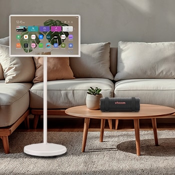 LG StanbyME 2 schermen weergegeven in een moderne woonkamer. Er staat een StanbyME 2 op een standaard, de ene hangt aan de muur en de andere staat op een tafel met behulp van de foliohoes.