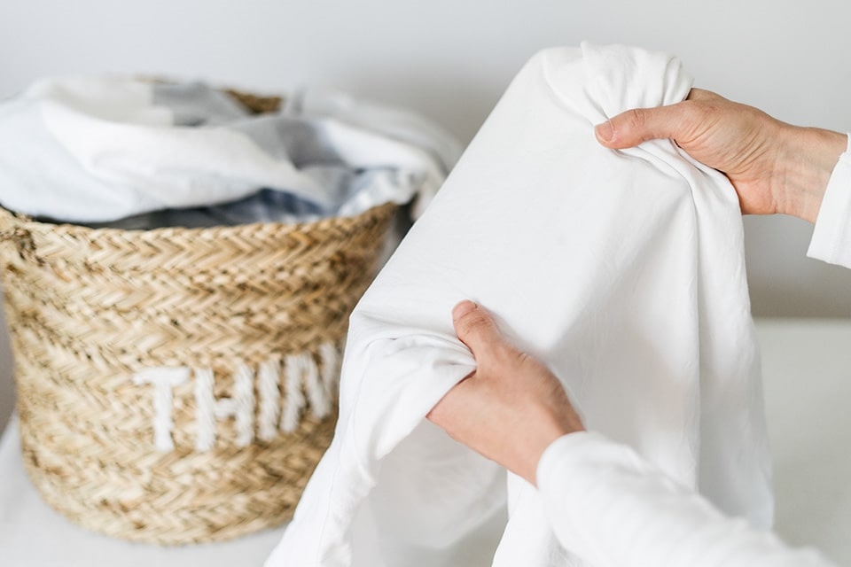 Vers gewassen witte kleding, met een wasmand gevuld met kleding op de achtergrond