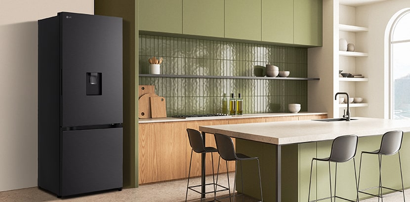 The side view of lg bottom freezer refrigerator with water dispenser in a kitchen with green cabinets and a stylish island.