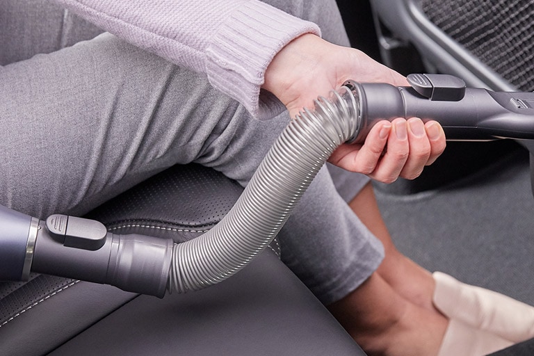 Four images: the first is the hard dirt tool getting dirt from a car carpet, the second is the flexible crevice tool reaching behind a table, the third is the multi angle tool getting dust from a top shelf, and the fourth is the flexible hose extension getting a narrow space in the car.