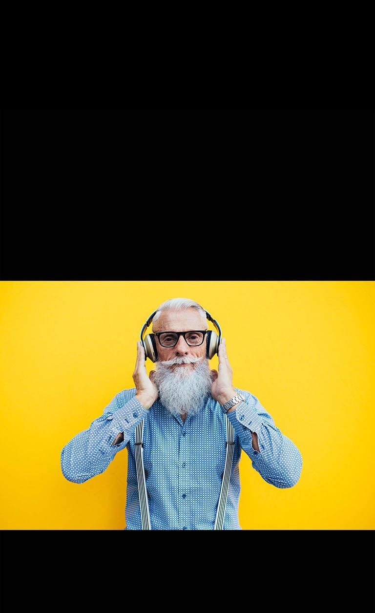 Un abuelo está parado frente a una pared amarilla, con auriculares.
