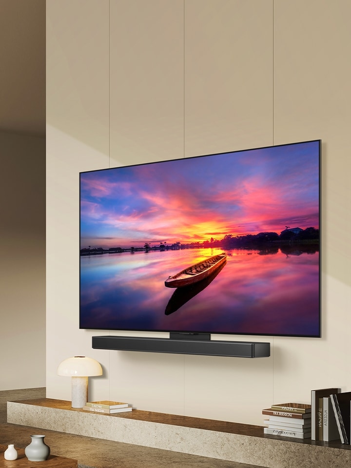 Una imagen de LG OLED C4 orientada 45 grados hacia la izquierda que muestra una hermosa puesta de sol con un barco en un lago, mientras el televisor está conectado a una barra de sonido LG a través del soporte Synergy en un espacio habitable minimalista.