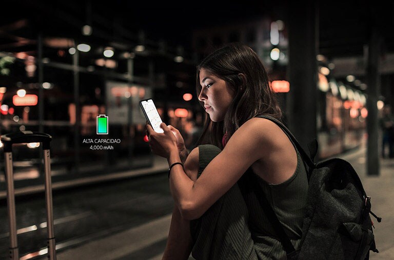 Mujer que navega por internet en su teléfono inteligente tarde en la noche en la estación de metro con suficiente batería