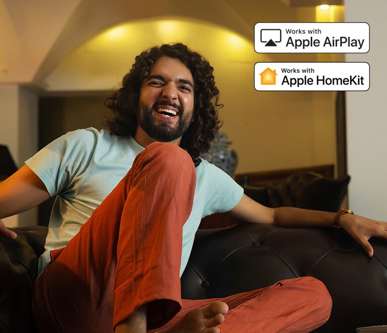 Un hombre está mirando algo muy feliz. Se muestran el logotipo de Apple AirPlay y el logotipo de Apple HomeKit en la esquina superior derecha de la imagen.