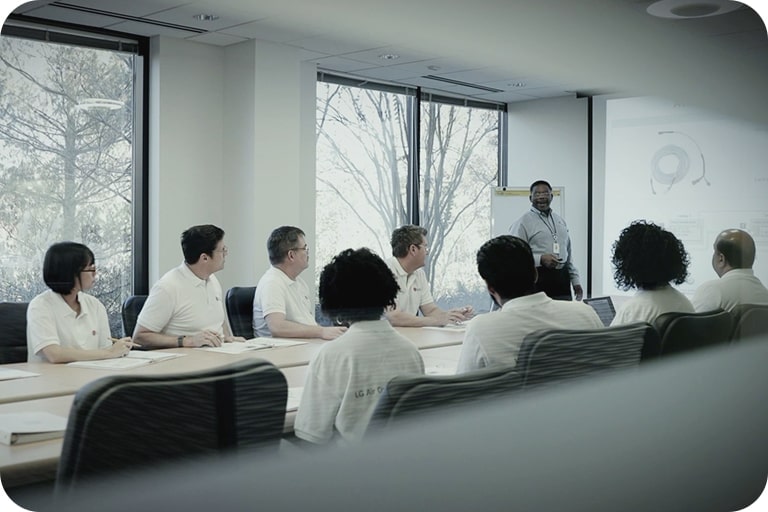 A group of professionals is seated around a table in a conference room, listening to a presenter at the front speaking about the LG HVAC industry.