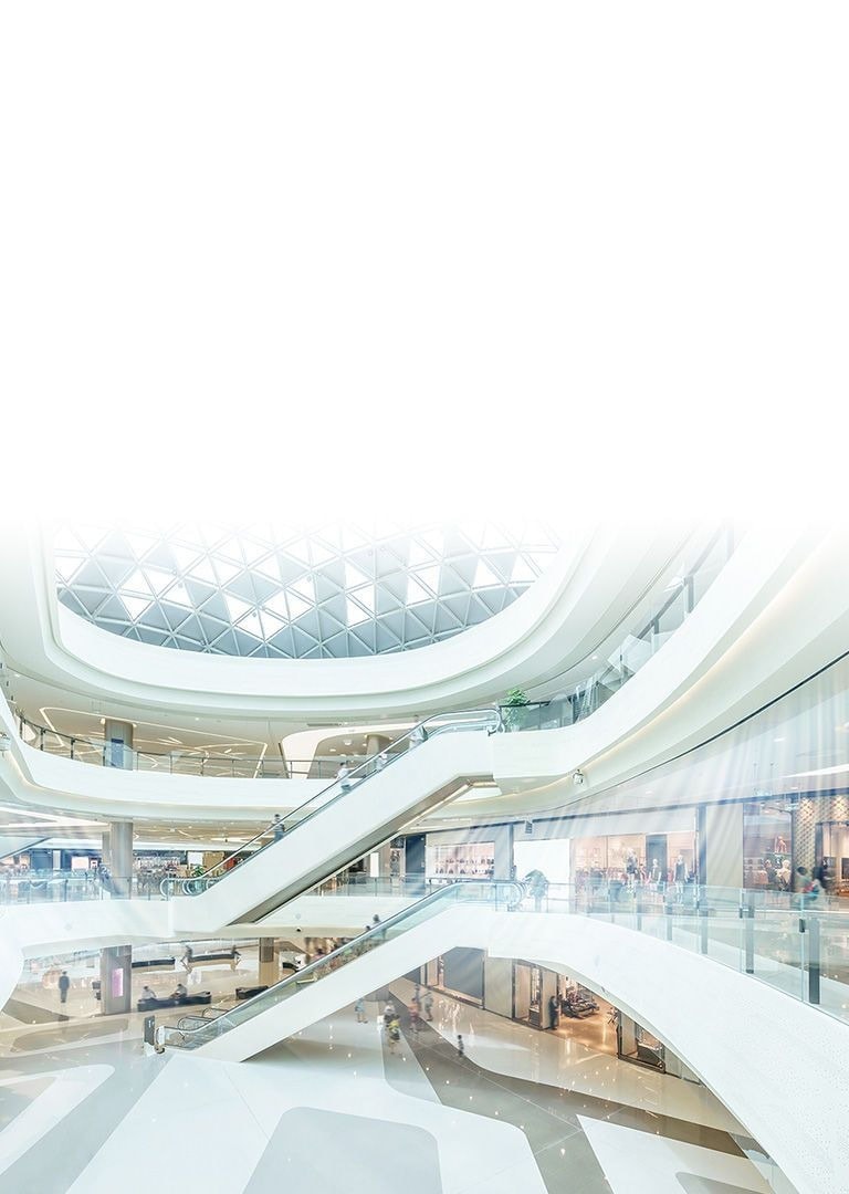 Ceiling concealed ducts supply blue-colored air stream in a large three-storied atrium building with multiple indoor stores and long escalators.