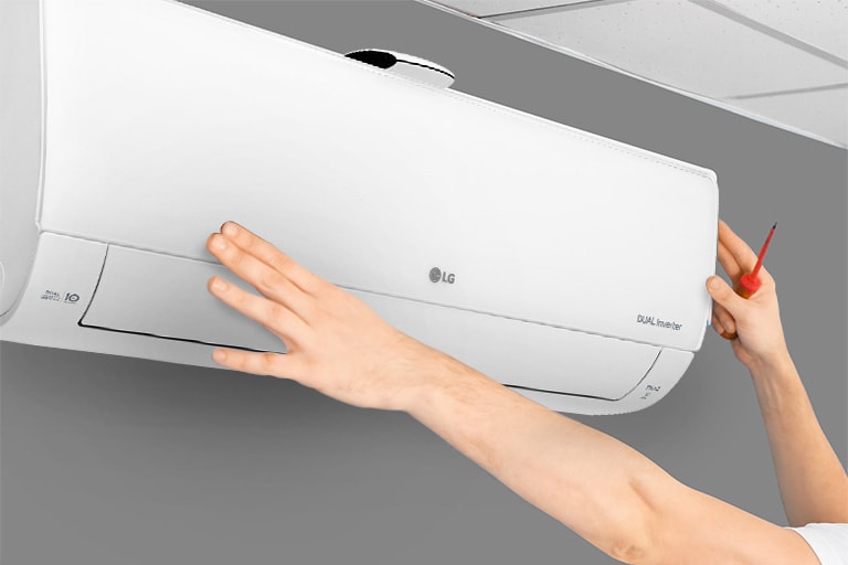 The side view of the air conditioner can be seen on the wall. Two hands are reaching up, one holding a tool, showing the ease of installation.