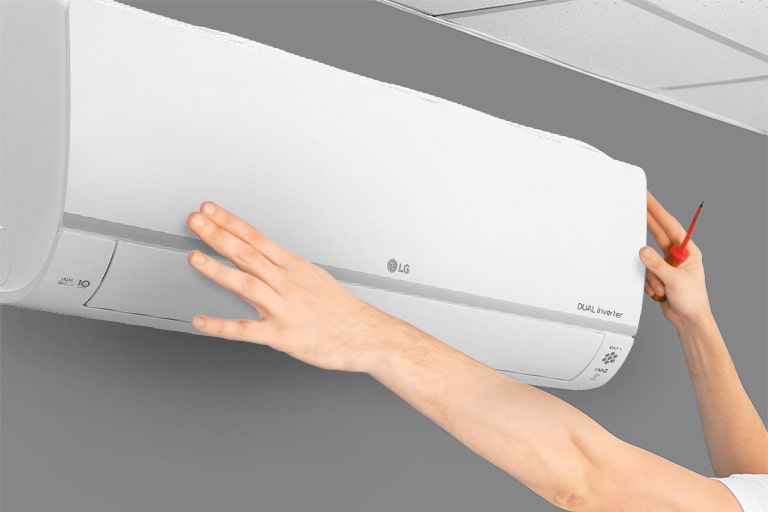 The side view of the air conditioner can be seen on the wall. Two hands are reaching up, one holding a tool, showing the ease of installation.