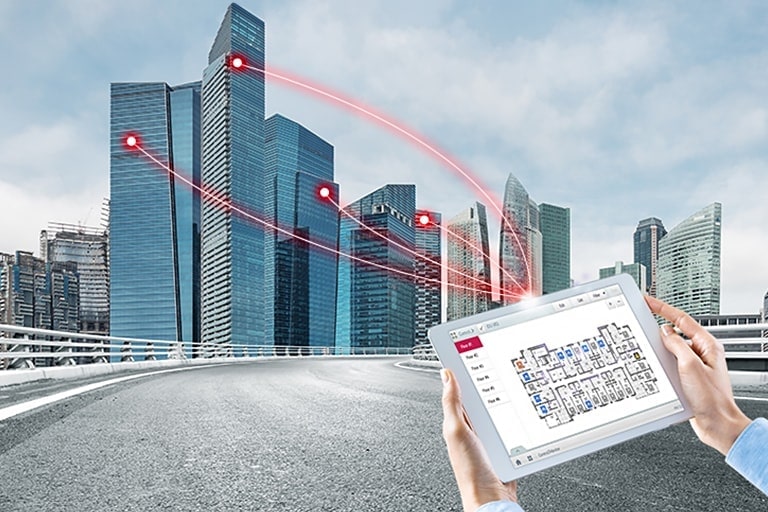 A person holds a tablet displaying a control solution. Four red lines extend from the tablet, connecting to buildings on the left.