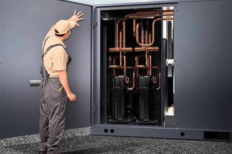 A man is holding the large, gray door of the LG Inverter Single Package, which is adorned with a series of bronze pipes and equipped with a motor.