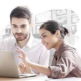 Two coworkers are gathered together, discussing while looking at a laptop screen. 