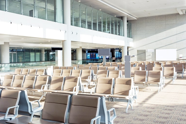 Back-to-back chairs in a large building. Glass wall reveals second floor, concrete wall has eight ventilation holes.