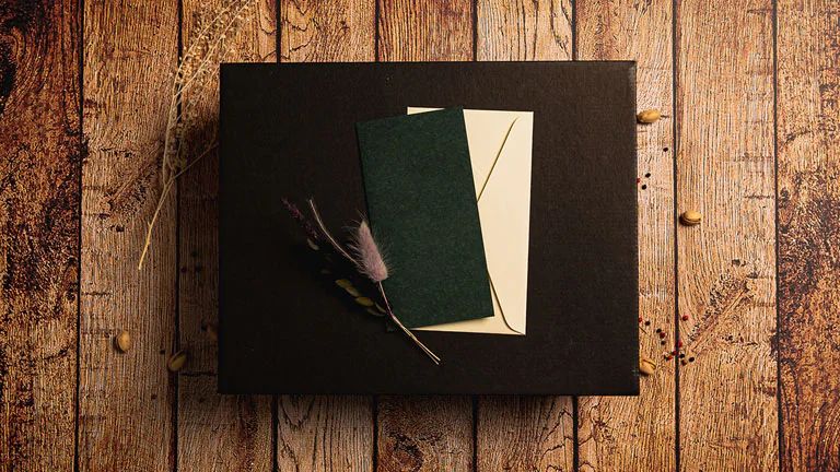 Centered on a wooden panel, a brown rectangle hosts a green notepad and envelope.