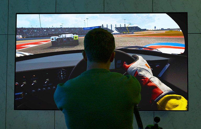 A man is sitting in a racing seat in front of a large TV playing a racing game.