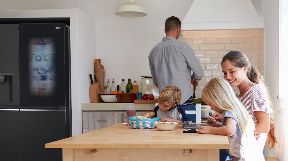 The whole family is sitting at the table preparing a meal. InstaView refrigerator installed on one side of the kitchen is creating cool air quickly.