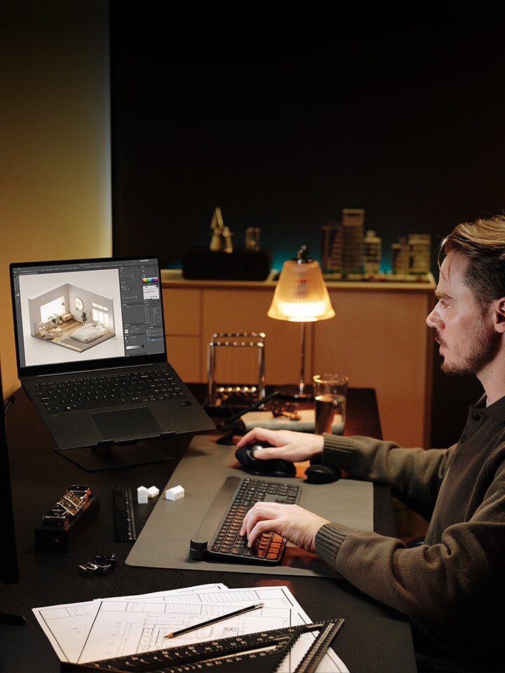 An image of a man sitting at a desk, sketching a 3D model on his laptop.