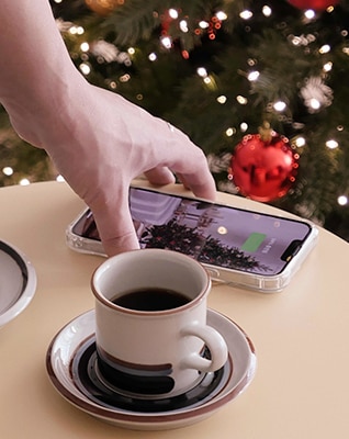 Using the charging function, a cell phone is placed on top of the product. There is a coffee cup next to it, showing it being used like a table.