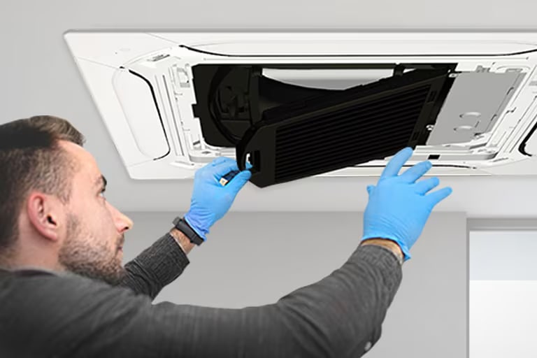 A man wearing blue nitrile gloves is replacing the black filter in an installed LG Dual Vane Cassette.
