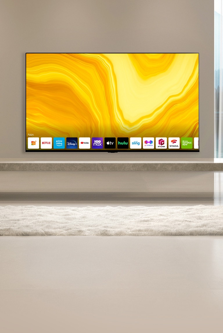 Ekran główny przewija się w dół i pojawia się wiszący na ścianie w ciepło urządzonym pokoju gościnnym telewizor z wyświetlonym ekranem głównym. 