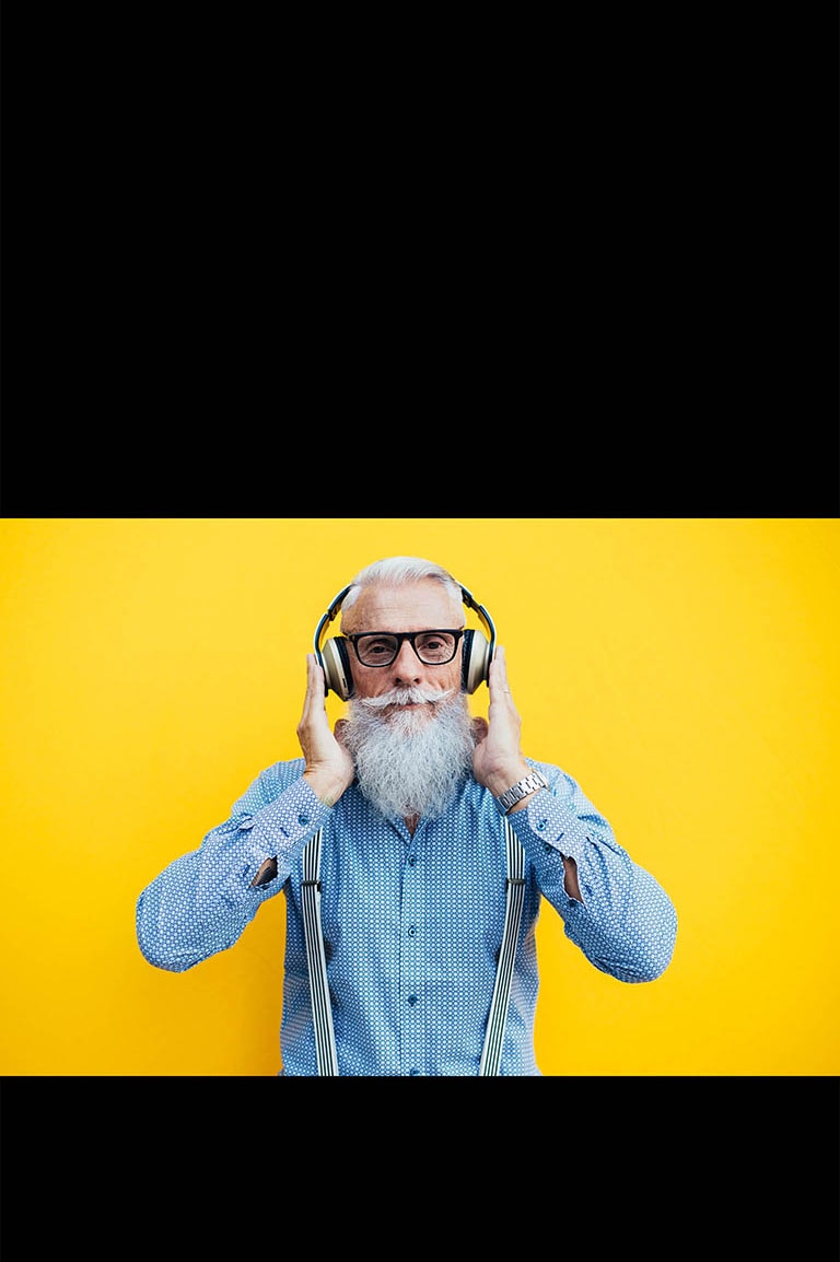 Dziadek stoi przed żółtą ścianą i ma na głowie słuchawki.