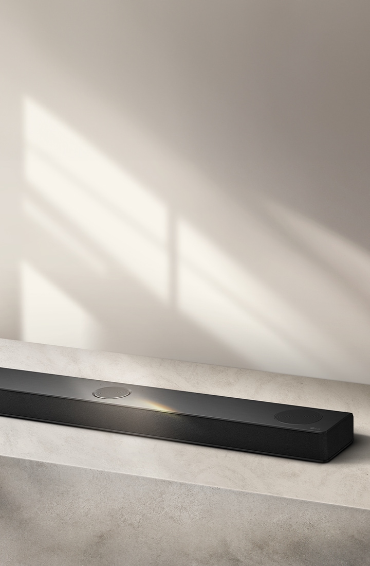 LG Soundbar numa superfície cinzenta contra um fundo cinzento em perspetiva aérea angular.