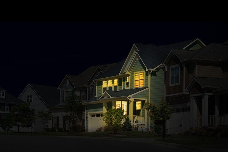 A row of houses in complete darkness with one lit up, indicating the Energy Solar System's use as a backup during a blackout.