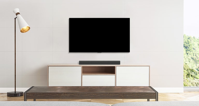 Uma TV, barra de som e subwoofer colocados numa sala de estar simples.