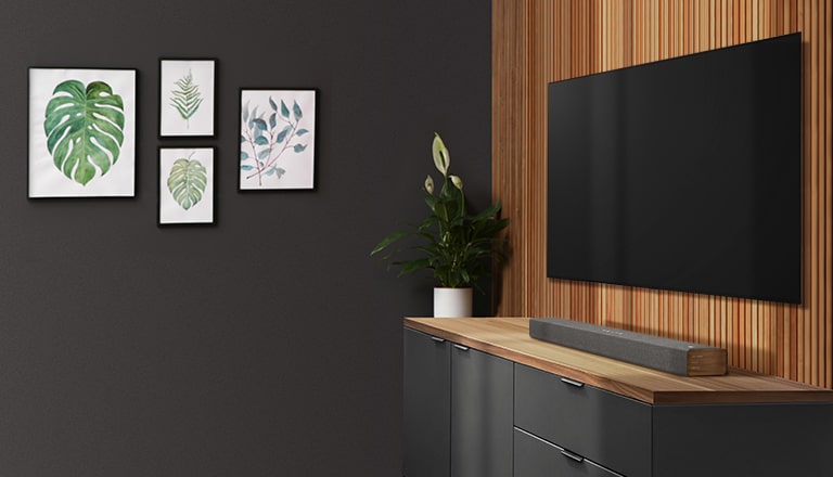 A TV e a barra de som numa parede em madeira. Há quatro molduras numa parede escura.
