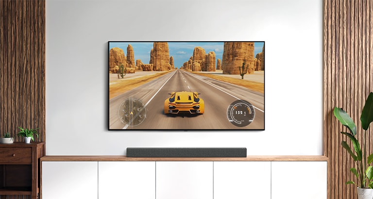 Há uma TV e uma barra de som numa sala de estar. Um jogo de corridas está no ecrã da TV (ver vídeo).