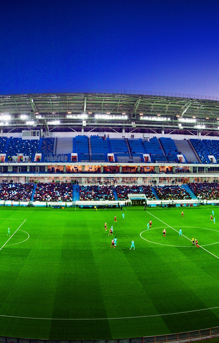 Vista panorâmica de um estádio de futebol cheio de público e um jogo a decorrer.