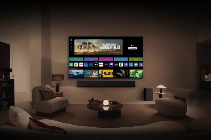 A close-up of an LG TV screen showing the buttons Home Office, Game, and Music over a banner for Masters of the Air zooms out to show the TV mounted on a wall in a living room. The following logos are displayed on the TV screen in the image: LG Channels, Netflix, Prime Video, Disney TV, Apple TV, YouTube, Spotify, Twitch, GeForce Now and Udemy.	