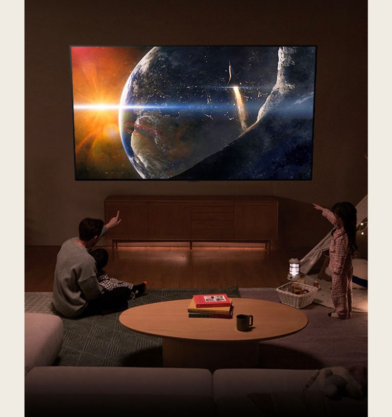 تجلس عائلة على أرضية غرفة معيشة منخفضة الإضاءة بجوار طاولة صغيرة، وتنظر إلى تلفزيون LG TV المثبت على الحائط والذي يُظهر الأرض من الفضاء.