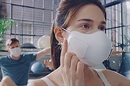 A video opens with a yoga class. One of the people in the class wears the PuriCare Wearable Air Purifier while the rest of the students wear regular cloth masks. The students stretch up and the camera focuses on a man wearing a normal mask who moves his mask below his nose and mouth as he struggles to breathe and work out. The background blurs and the words &quot;Breathing shouldn't be an exercise in frustration&quot; appear. Next focus moves to the woman wearing the PuriCare mask. As she begins to breathe harder, she taps the side of the mask twice to increase air filtering. The mask becomes invisible with only the fans showing to show how she can easily breathe through the mask even while working out. The words &quot;DUAL Fans activate in sync with your breathing to help take in air&quot; appear at the bottom. As the woman inhales, the fans glow blue and as she exhales the fans go dark easily keeping up with her. The students lie down to stretch and the zoom pulls out showing her PuriCare mask once again and all of the other students wearing cloth masks. Next a white background and then the words &quot;Technology that lets you breathe easy&quot;. Finally the words disappear and the LG PuriCare Wearable Air Purifier logo ends the video.