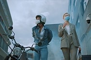 A video opens with a woman disembarks from her motorcycle in a busy city. She's wearing the PuriCare Wearable Air Purifier and pedestrians passing are wearing normal cloth masks. A man passes by with the cloth  mask beneath his chin and a woman with a cloth mask walks up and stops. Her glasses have fogged up and she takes them off and stretches her neck and takes off her cloth mask to relax her ears. The background blurs and the words &quot;All day discomfort doesn't have to be your new normal&quot; appear. The focus goes back to the woman in the PuriCare mask who takes off her helmet. The camera focuses on the comfort aspects of the mask. The mask goes invisible and the Face Guard can be seen around the woman's mouth. The words &quot;Flexible Face Guard hugs the contours of your face while minimizing air leakage&quot; appears on the bottom. The camera moves down to show the chin vent. The words &quot;Easy exhalation vent and soft ear straps provide all day comfort&quot; appear on the bottom. The focus moves to the ear straps resting comfortably around the woman's ears. The camera moves out to show the woman wearing glasses that haven't fogged and the mask is not invisible anymore. Next a white background and then the words &quot;Technology that lets you breath easy&quot;. Finally the words disappear and the LG PuriCare Wearable Air Purifier logo ends the video.