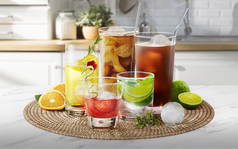 Various glasses of different sizes holding different drinks with round ice cubes are on a kitchen counter.