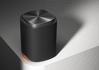 LG Sound Suite-högtalare på en bordsskiva med ett rundat mörk hölje och en mjuk orange glöd vid basen.